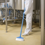 Worker cleaning factory floor with blue squeegee